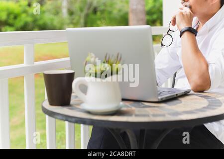 Zugeschnittenes Bild eines Geschäftsmannes, der seine Brille mit Laptop auf dem Tisch hält. Stockfoto