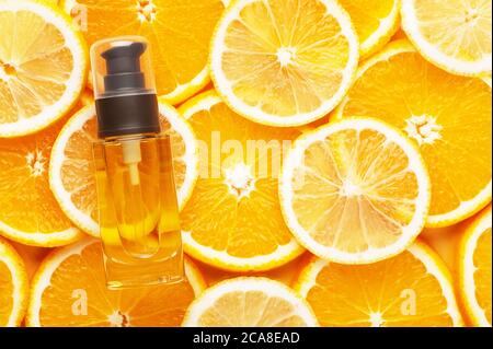 Draufsicht auf unbranded Glasbehälter mit Öl für Haar. Transparente Flasche mit Spender. Saftige Scheiben von Orange und Zitrone auf dem Hintergrund. Werbung Stockfoto