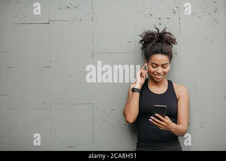 Geräte für den Sport. Happy african american Mädchen mit Kopfhörer, Fitness-Tracker, schaut auf Smartphone und wählt Musik Stockfoto
