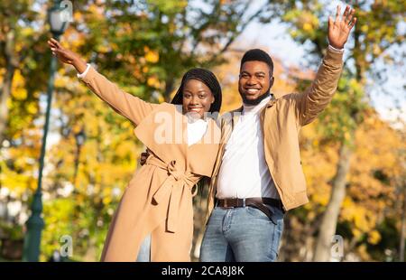 Stilvolles schwarzes Paar posiert mit erhobenen Händen im Herbstpark Stockfoto