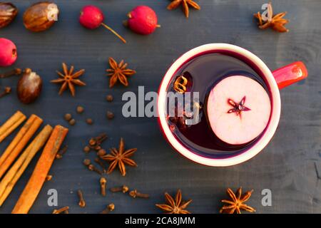 Weihnachtlicher Glühwein mit Gewürzen und Apfel in rotem Becher auf Holzhintergrund. Zimt, Muskatnuss, Sternanis, Nelken. Stockfoto