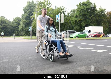 Ehemann rollt einen Rollstuhl mit einer jungen Frau Stockfoto