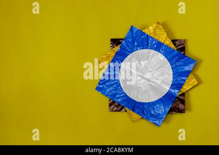 Drei quadratische Stücke farbige Folie auf gelb. Folienstücke braun, blau und gelb mit einem weißen Kreis. Abstrakter Hintergrund. Flach liegend. Stockfoto