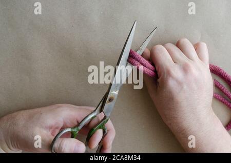 Die Hand eines erwachsenen kaukasischen Mannes schneidet das rote Seil mit einer alten Metallschere. Retro-Handwerkzeuge. Manuelle Arbeit. Handwerk. Draufsicht in einem Winkel. Stockfoto