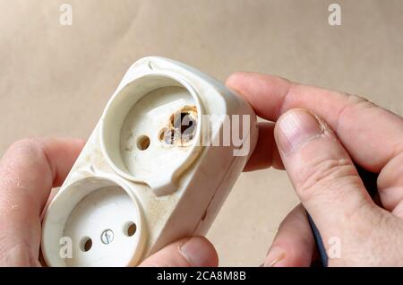 Ein Elektriker demonstriert eine verbrannte Steckdose. Weißes Verlängerungskabel nach Kurzschluss in der männlichen Hand. Elektrische Sicherheit. Stockfoto