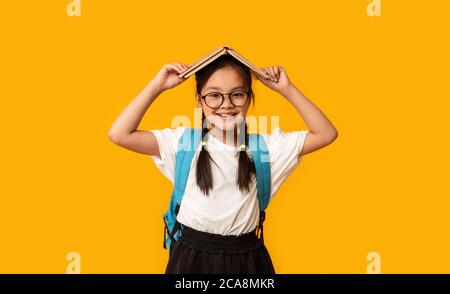 Liebenswert Koreanisch Schulmädchen Holding Buch Auf Kopf Posieren, Studio Shot Stockfoto