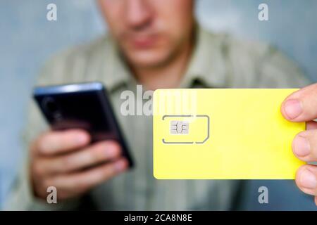 Der Mensch hält eine gelbe SIM-Karte und ein Mobiltelefon in der Hand. Freier Platz für Design und Text Stockfoto