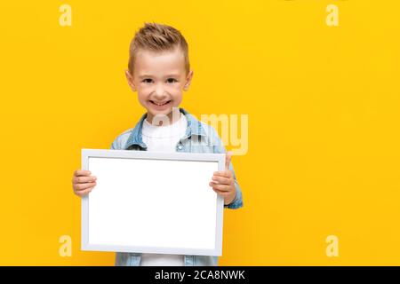 Glücklich lächelndes Kind hält weißen Rahmen mit Kopieplatz für Text Zertifikat oder Diplom Stockfoto