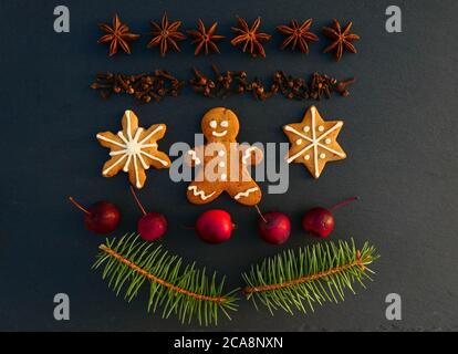 Weihnachtsdekoration Hintergrund mit Lebkuchen Cookies. Fichtenzweige, Gewürze und Äpfel auf schwarzem Steinbrett. Stockfoto