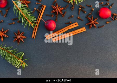 Weihnachten natürliche Dekoration Hintergrund. Fichtenzweige, Gewürze und Äpfel auf schwarzem Stein. Stockfoto
