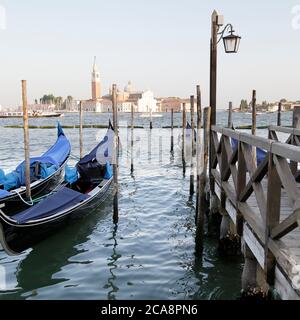 Im Vordergrund mehrere Gondeln und auf der rechten Seite eine kleine hölzerne Pier im Hintergrund die Kirche und Kloster von San Giorgio Maggiore, Venedig, Es Stockfoto