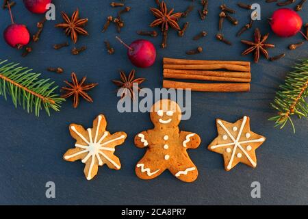 Weihnachtsdekoration Hintergrund mit Lebkuchen Cookies. Fichtenzweige, Gewürze und Äpfel auf schwarzem Steinbrett. Stockfoto
