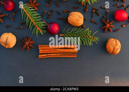 Weihnachten natürliche Dekoration Hintergrund. Fichtenzweige, Gewürze und Äpfel auf schwarzem Stein. Stockfoto