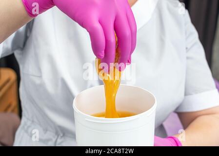 Close up goldenen flüssigen Zucker in einem weißen Glas in den Händen eines Enthaarungsmeisters Stockfoto