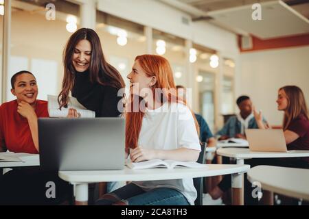 Studentin im Gespräch mit Mitschülern und lächelnd im Hörsaal. Studenten im Klassenzimmer nach der Vorlesung. Stockfoto