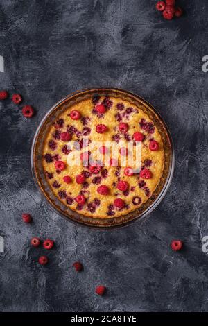 Süßer leckerer Kuchen mit Gelierobst und frischen Himbeerfrüchten in Backform, dunkler Steinbeton Hintergrund, Draufsicht Stockfoto