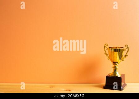 Champion goldene Trophäe auf Holztisch mit orangefarbenem Hintergrund Stockfoto