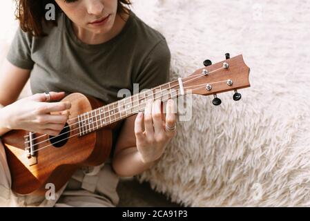 Eine schöne Frau spielt die kleine Gitarre zu Hause. Ein junges Mädchen spielt Ukulele während der Selbstisolation. Stockfoto