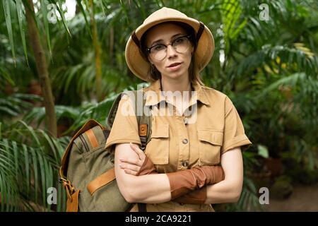 Nahaufnahme Porträt einer Botanistin in Safari-Stil im Gewächshaus gekleidet. Naturforscher in Khaki-Kleidung, Lever Handschuhe mit Rucksack Blick auf die Kamera, Stockfoto