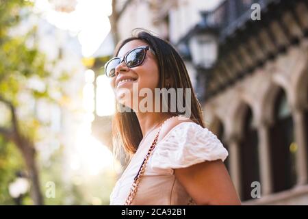 Frau mit Sonnenbrille lächelt, als sie durch die Stadt geht Stockfoto
