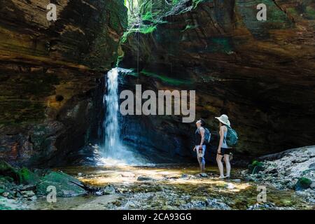 Zwei junge Wanderer Canyoning einen Fluss hinauf und stehen in einer Höhle im Regenwald, vor einem unberührten Wasserfall, Minas Gerais, Brasilien, Südamerika Stockfoto