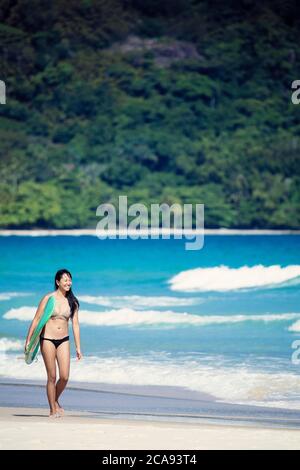 Strandaufnahme eines japanischen Brasilianers (Nipo-brasileiro) in einem Bikini, der ein Surfbrett mit der brasilianischen Flagge trägt, Brasilien, Südamerika Stockfoto