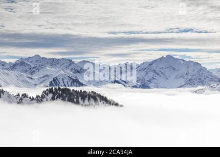 Schneebedeckte Berge mit Inversion Valley Nebel und Bäume in Nebel gehüllt. Malerische verschneite Winterlandschaft in Alpen, Allgau, Kleinwalsertal, Bayern Stockfoto
