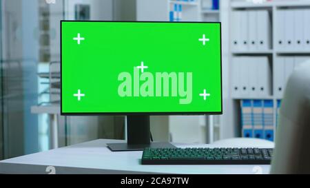 Dolly Aufnahme des Computers mit grünem Bildschirm im privaten Krankenhaus und Personal trägt Uniform im Hintergrund. PC mit leerem und kopierbarem grünen Bildschirm, der auf dem Display des Medizinspezialisten im Klinikschrank zur Verfügung steht. Stockfoto