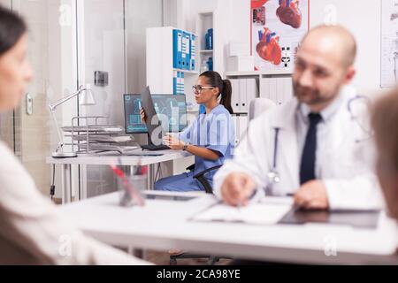 Krankenschwester in der Krankenhausniederlassung mit Röntgenbild. Arzt trägt weißen Mantel während der Konsultation der jungen Frau und behinderten erwachsenen Mutter im Rollstuhl. Stockfoto