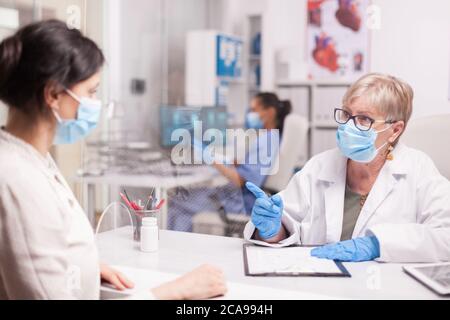 Oberarzt mit Gesichtsmaske gegen Coronavirus während der Konsultation mit weiblichen Patienten. Krankenschwester trägt blaue Uniform. Stockfoto