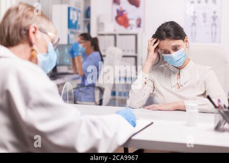 Junge Frau mit Schutzmaske gegen covid-19 Weinen während der Untersuchung mit Arzt im Krankenhauszimmer. Stockfoto