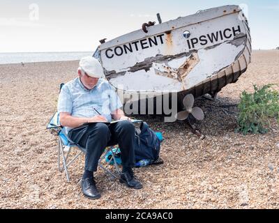 Aldeburgh, Suffolk, Großbritannien. August 2020. Ein Künstler ist zufrieden, am Kiesstrand an der Nordsee zu sitzen und zu zeichnen. Es war ein warmer Sommertag mit einer steifen Brise, da der aktuelle heiße Zauber im Osten Englands weitergeht. Kredit: Julian Eales/Alamy Live Nachrichten Stockfoto