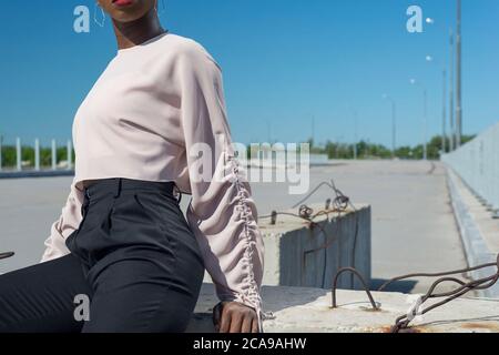 Nahaufnahme Porträt modische dunkelhäutige Mädchen, afrikanisches Mädchen in einer Bluse und Business-Hosen, posiert. Vor dem Hintergrund des blauen Himmels. Modisch b Stockfoto