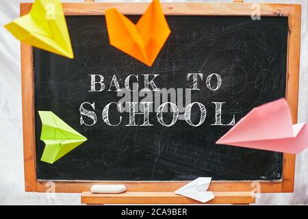 'Back to School' Inschrift, farbige Papierflugzeuge fliegen in der Nähe der Schulbank, Universität, Hochschule Stockfoto