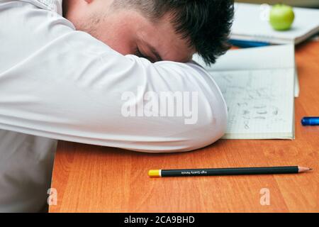 Ein Mann schläft auf einem Tisch mit einem Notizbuch und einem Bleistift Universität, Hochschule Stockfoto
