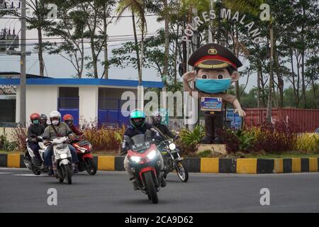 Malang, Ost-Java, Indonesien. August 2020. Eine Gruppe Motorradfahrer fährt über die Polizeistatue. Eine Polizeistatue trägt Facemask und bringt ein Schild mit dem Text "Wear Facemask, Maintain the Distance, Stay Home" in Bahasa Indonesia Sprache gemischt mit malangesischer Sprache als Gesundheitsprotokolle Erinnerung für die Verkehrsteilnehmer, um Covid-19 Coronavirus von zu kontrollieren. (Bild: © Dicky BisinglasiZUMA Wire) Stockfoto