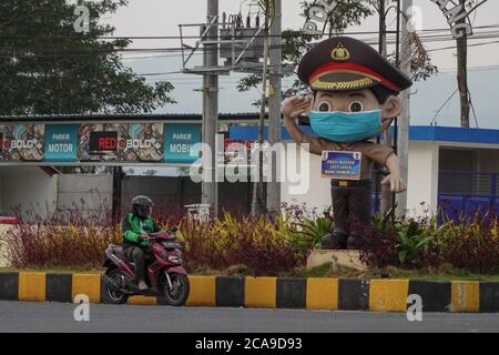 Malang, Ost-Java, Indonesien. August 2020. Ein Online-Motorrad-Taxifahrer fährt über die Polizeistatue. Eine Polizeistatue trägt Facemask und bringt ein Schild mit dem Text "Wear Facemask, Maintain the Distance, Stay Home" in Bahasa Indonesia Sprache gemischt mit malangesischer Sprache als Gesundheitsprotokolle Erinnerung für die Verkehrsteilnehmer, um Covid-19 Coronavirus von zu kontrollieren. (Bild: © Dicky BisinglasiZUMA Wire) Stockfoto