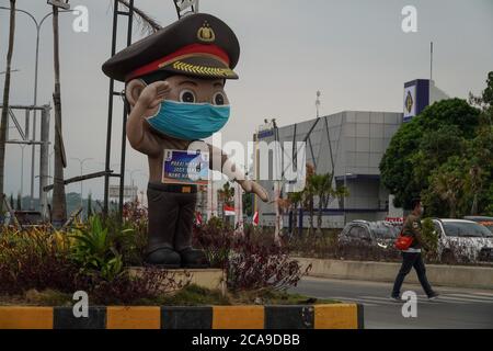 Malang, Ost-Java, Indonesien. August 2020. Ein Mann geht neben die Polizeistatue. Eine Polizeistatue trägt Facemask und bringt ein Schild mit dem Text "Wear Facemask, Maintain the Distance, Stay Home" in Bahasa Indonesia Sprache gemischt mit malangesischer Sprache als Gesundheitsprotokolle Erinnerung für die Verkehrsteilnehmer, um Covid-19 Coronavirus von zu kontrollieren. (Bild: © Dicky BisinglasiZUMA Wire) Stockfoto