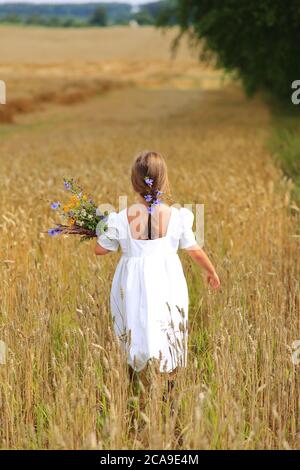 Kleines Mädchen mit einem Blumenstrauß in den Händen in einem Weizenfeld. Stockfoto