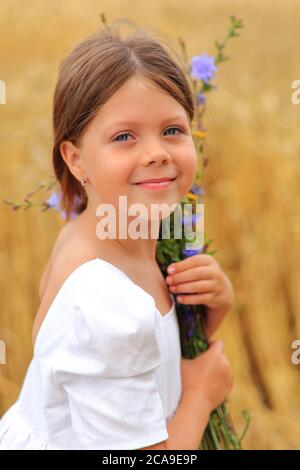 Kleines Mädchen mit einem Blumenstrauß in den Händen in einem Weizenfeld. Stockfoto