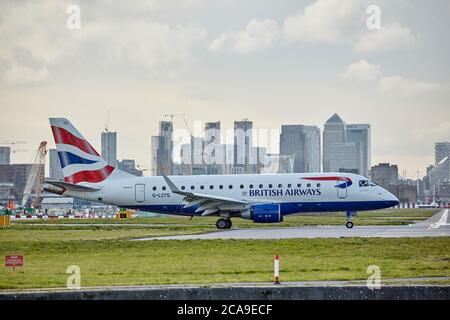 British Aiways Embrear 170 Flugzeug rollt am London City Airport mit der Londoner Skyline im Hintergrund. Stockfoto