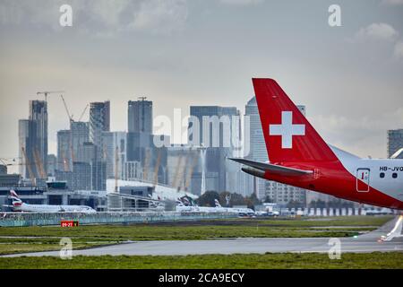 Schweif eines rollenden Swiss Air-Flugzeugs am London City Airport mit der Londoner Skyline im Hintergrund. Stockfoto