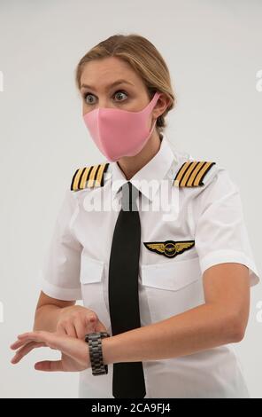 Wiltshire, England, Großbritannien. August 2020. Airline-Pilot überprüft ihre Armbanduhr und trägt eine Gesichtsmaske während der Covid-19-Sperre. Stockfoto