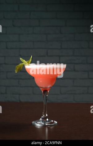 Rosafarbener Cocktail im Glas auf einem Holztisch gegen eine Ziegelwand. Fotos für Restaurants, Cafés und Barmenüs Stockfoto