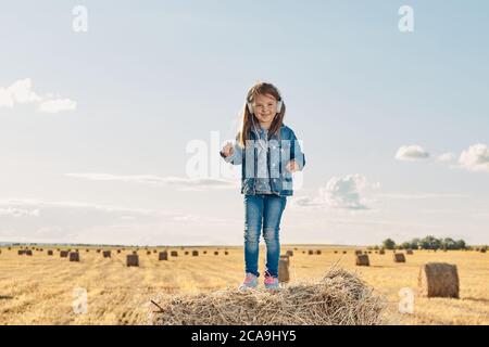 Ein nettes kleines Mädchen hört Musik und tanzt auf einem Heuhaufen. Hochwertige Fotos Stockfoto