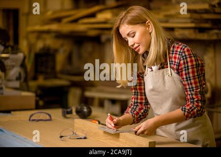 Portrait von professionellen Holzarbeiter Marken auf Holzstück, Frau machen handgemachte Möbel in der Werkstatt, genießen Sie die Arbeit allein Stockfoto