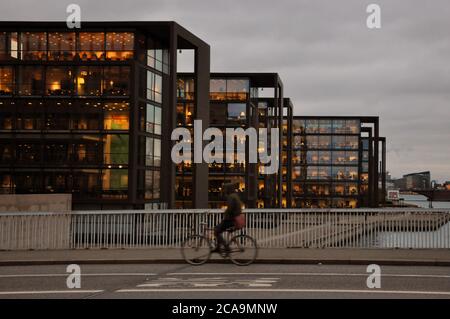 Eine Person fährt mit dem Fahrrad auf der Brücke vorbei und im Hintergrund befinden sich drei Gebäude. Dieses Foto wurde in Kopenhagen, Dänemark, aufgenommen. Stockfoto