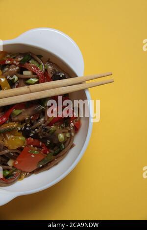 Eine Schüssel mit Wok Nudeln und Essstäbchen isoliert auf gelbem Hintergrund flach legen extreme Nahaufnahme. Das Bild enthält den Kopierbereich Stockfoto