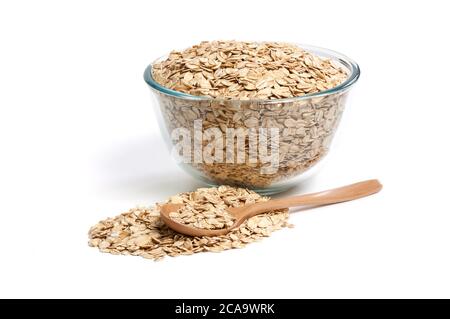 Haferflocken in Glasschüssel und Holzlöffel isoliert auf weißem Hintergrund. Hochauflösende Makro-Nahaufnahme von Haferflocken. Volle Schärfentiefe. Stockfoto