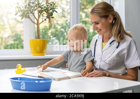 Angenehmer Arzt und Kind beobachten Buch zusammen am Schreibtisch in Klinik Büro. Kleiner Junge bei Kinderarzt Besuch Stockfoto